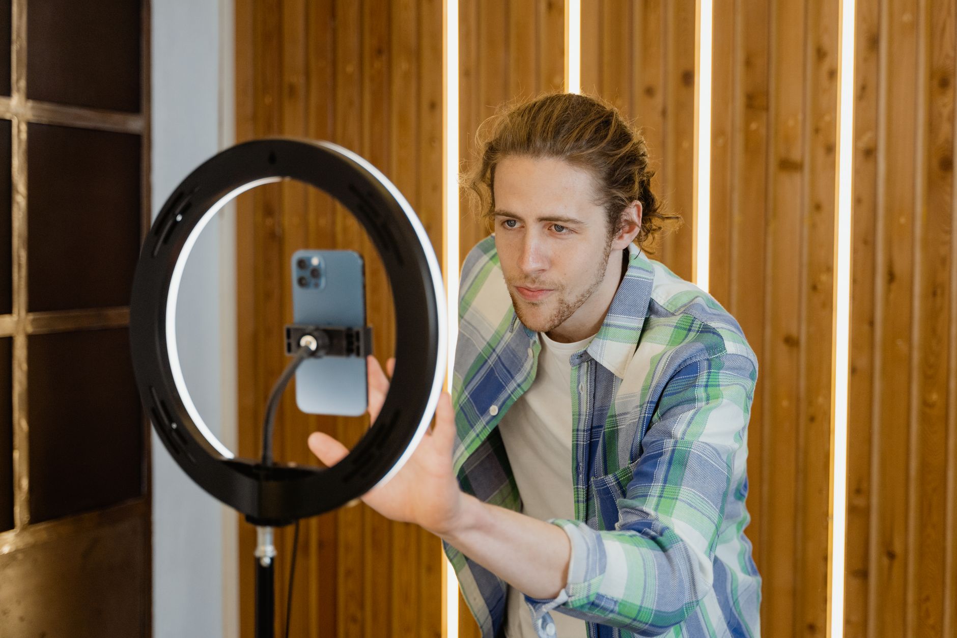 A young man sets up a smartphone and ring light for social media video recording, focusing on optimal lighting.