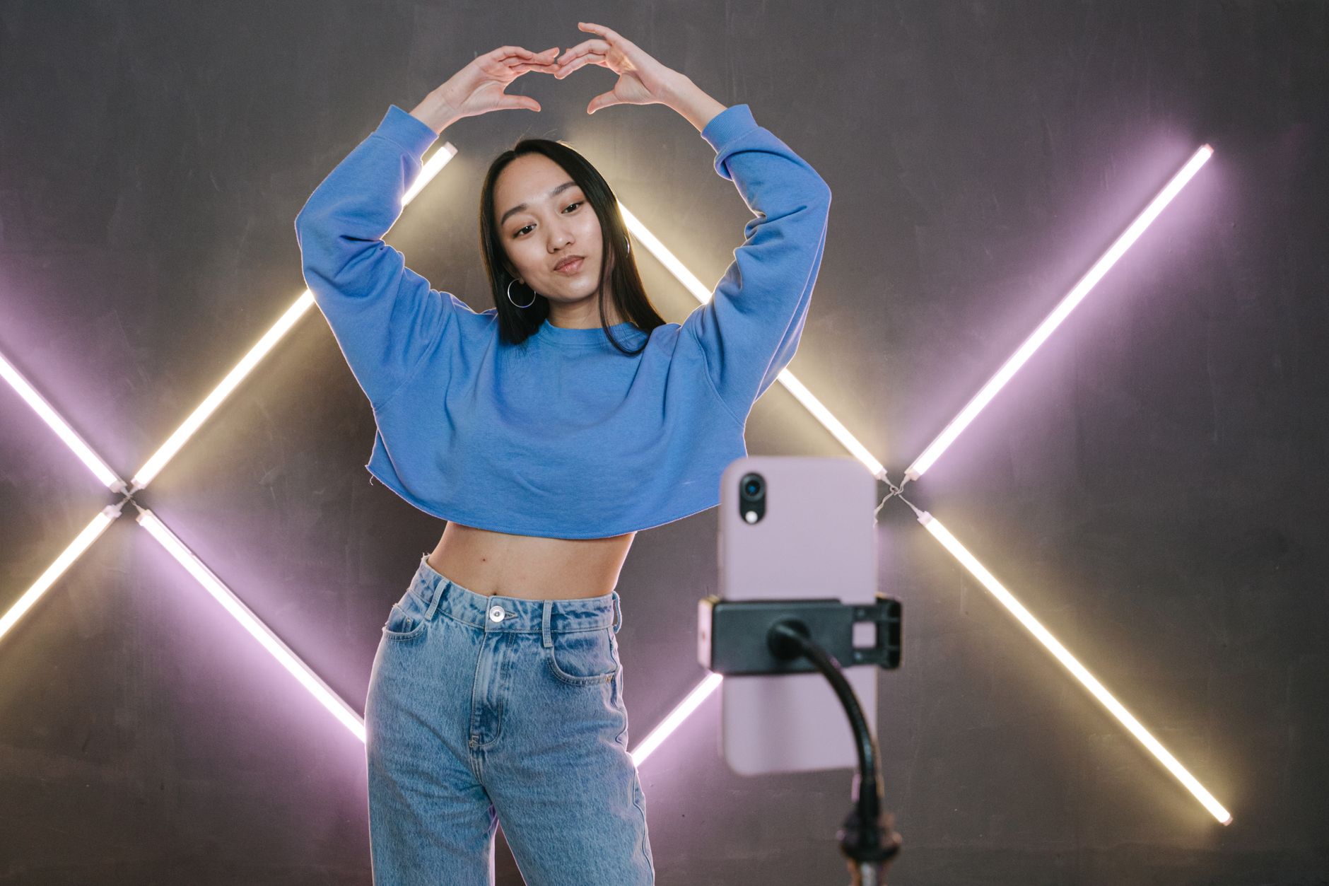 Fashionable young woman posing for a mobile shoot with neon lights in a studio.